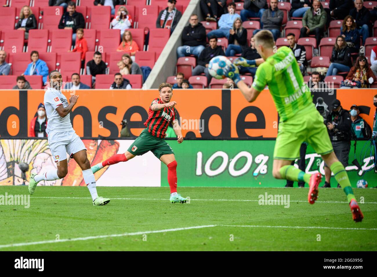 Augsburg, Germany. 28th Aug, 2021. Football: Bundesliga, FC Augsburg - Bayer Leverkusen, Matchday 3, WWK Arena. Goalkeeper Lukas Hradecky of Leverkusen (r) is able to keep out a ball from Robert Gumny of Augsburg (M). Leverkusen's Jonathan Tah defends on the left. Credit: Matthias Balk/dpa - IMPORTANT NOTE: In accordance with the regulations of the DFL Deutsche Fußball Liga and/or the DFB Deutscher Fußball-Bund, it is prohibited to use or have used photographs taken in the stadium and/or of the match in the form of sequence pictures and/or video-like photo series./dpa/Alamy Live News Stock Photo