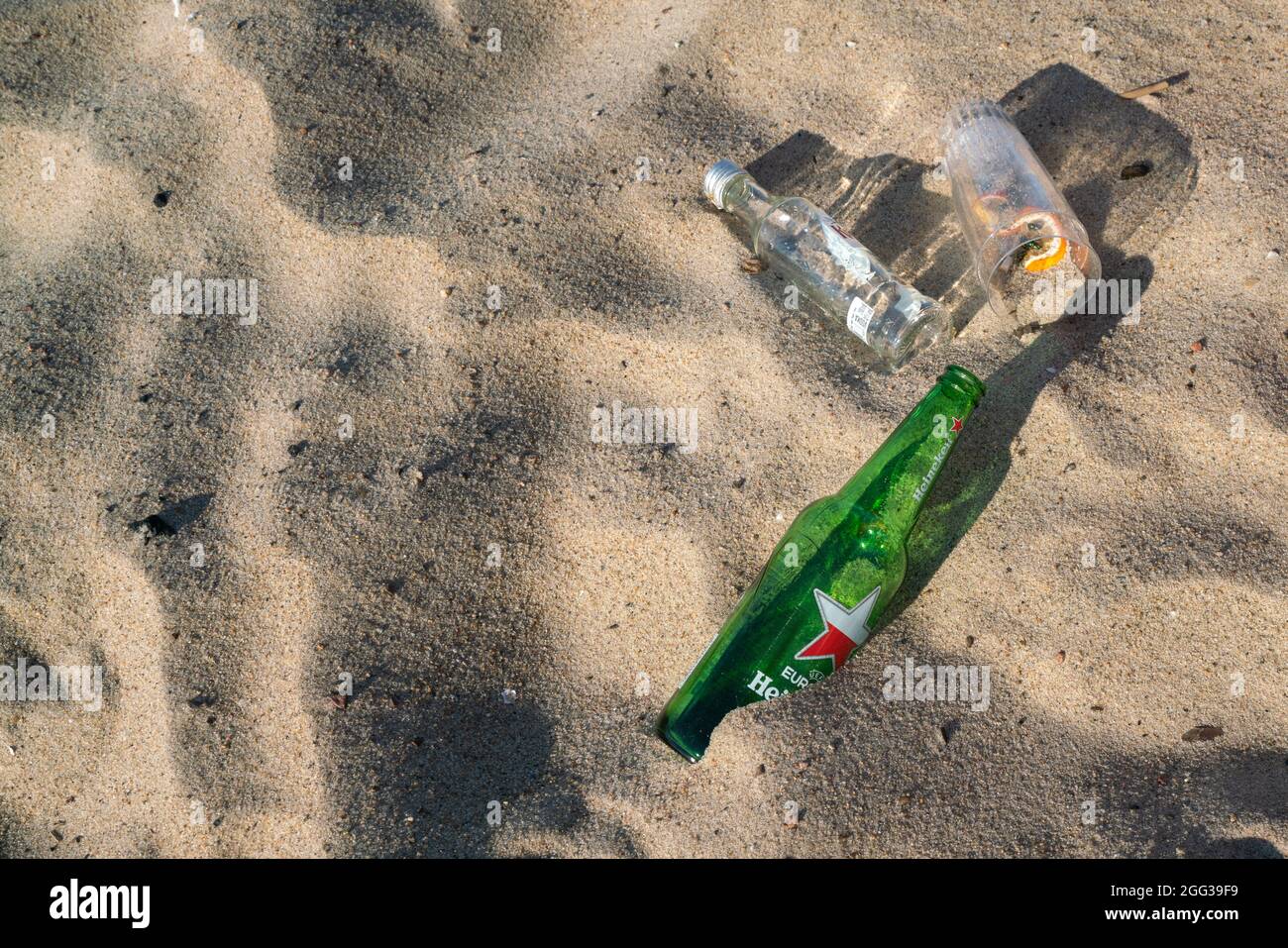 Hel, Poland - 08.02.2021: Detail shot of empty beer bottles and glasses lying on the beach sand in early morning after previous day party. Stock Photo