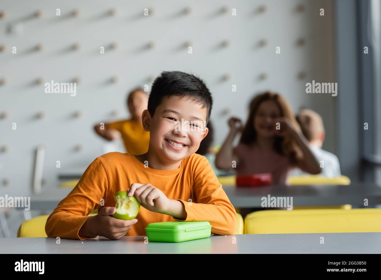 https://c8.alamy.com/comp/2GG3B50/happy-asian-kid-holding-with-fresh-apple-smiling-at-camera-near-blurred-children-in-school-canteen-2GG3B50.jpg