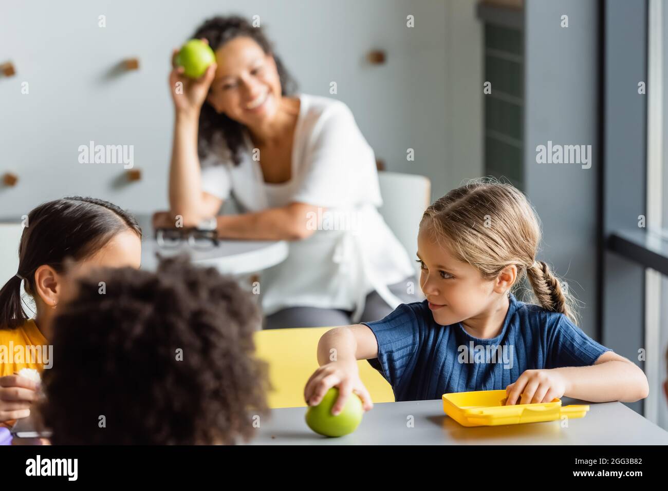 multiethnic kids having lunch in school canteen near teacher smiling on  blurred background Stock Photo - Alamy