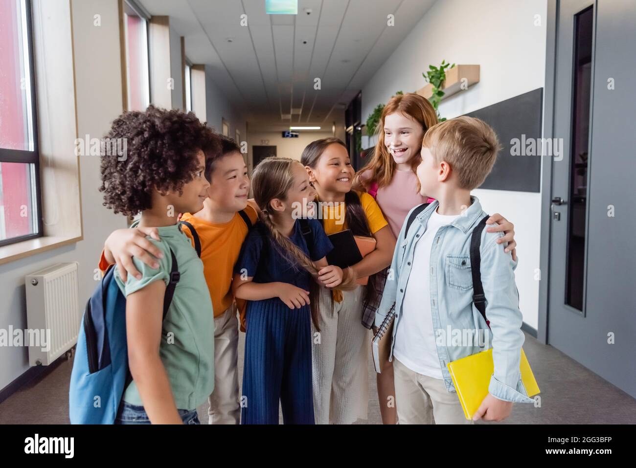 cheerful multicultural kids talking and hugging in school hall Stock Photo