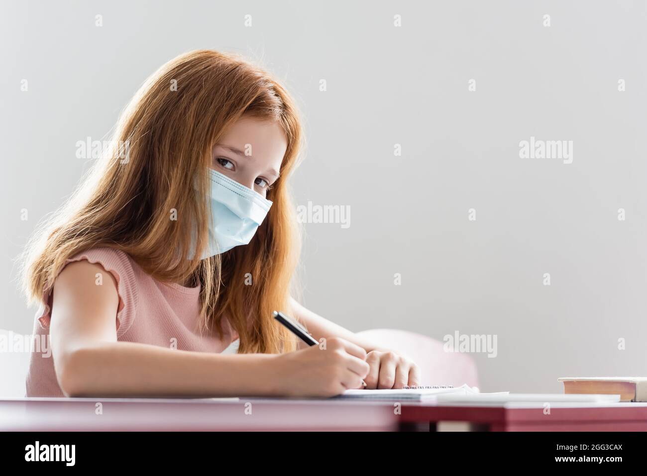 schoolgirl in medical mask writing during school lesson Stock Photo