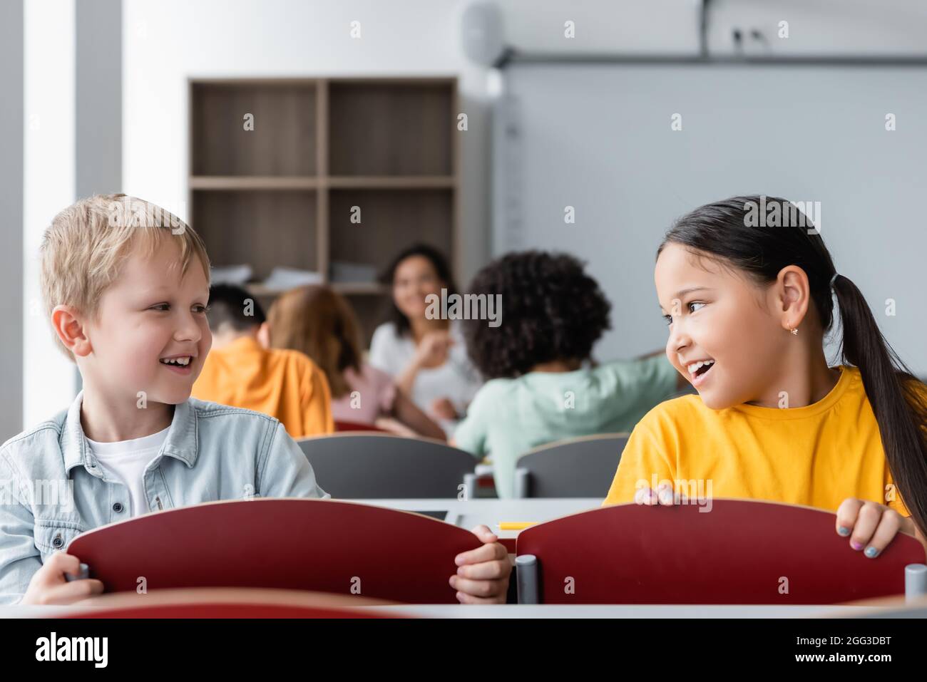 smiling interracial pupils talking during lesson in classroom Stock Photo