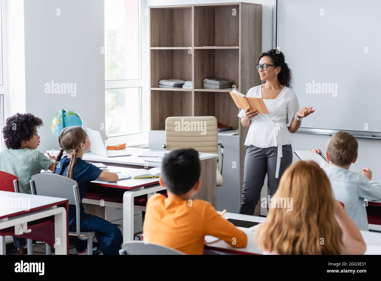 african american teacher pointing with hand while reading book in ...