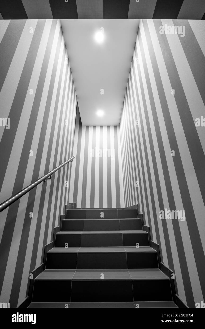 Vertical shot of gloomy lit staircase with vertical dark and white stripes on the walls. Concept for maze, labyrinth, mystery, secret chamber. Stock Photo
