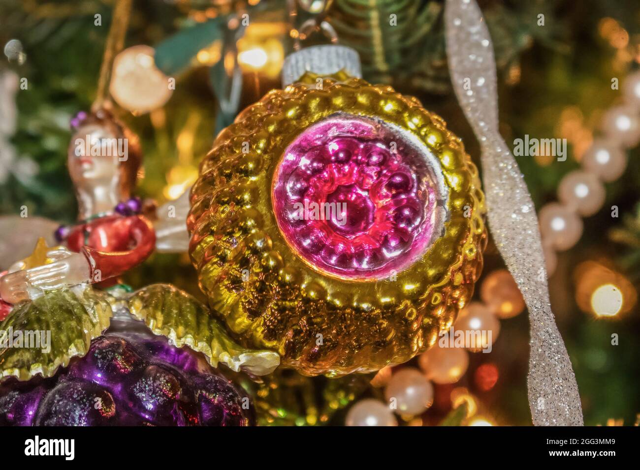 Retro Christmas ornament hanging on green Christmas tree with other decorations blurred behind Stock Photo