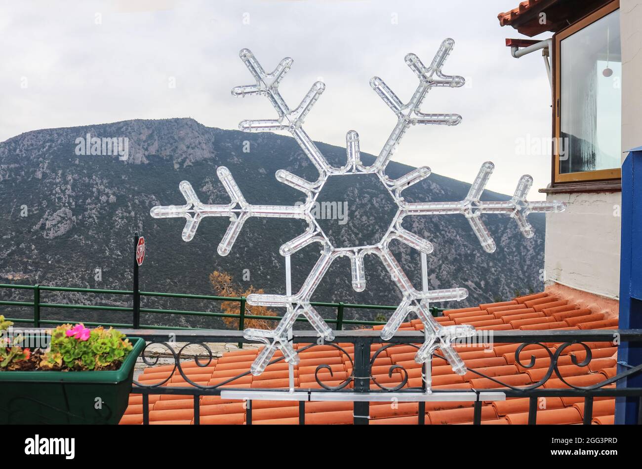Snowflake Christmas decoration on fence in Delphi Greece by tile roof and balcony overlooking deep valley and mountain in background Stock Photo