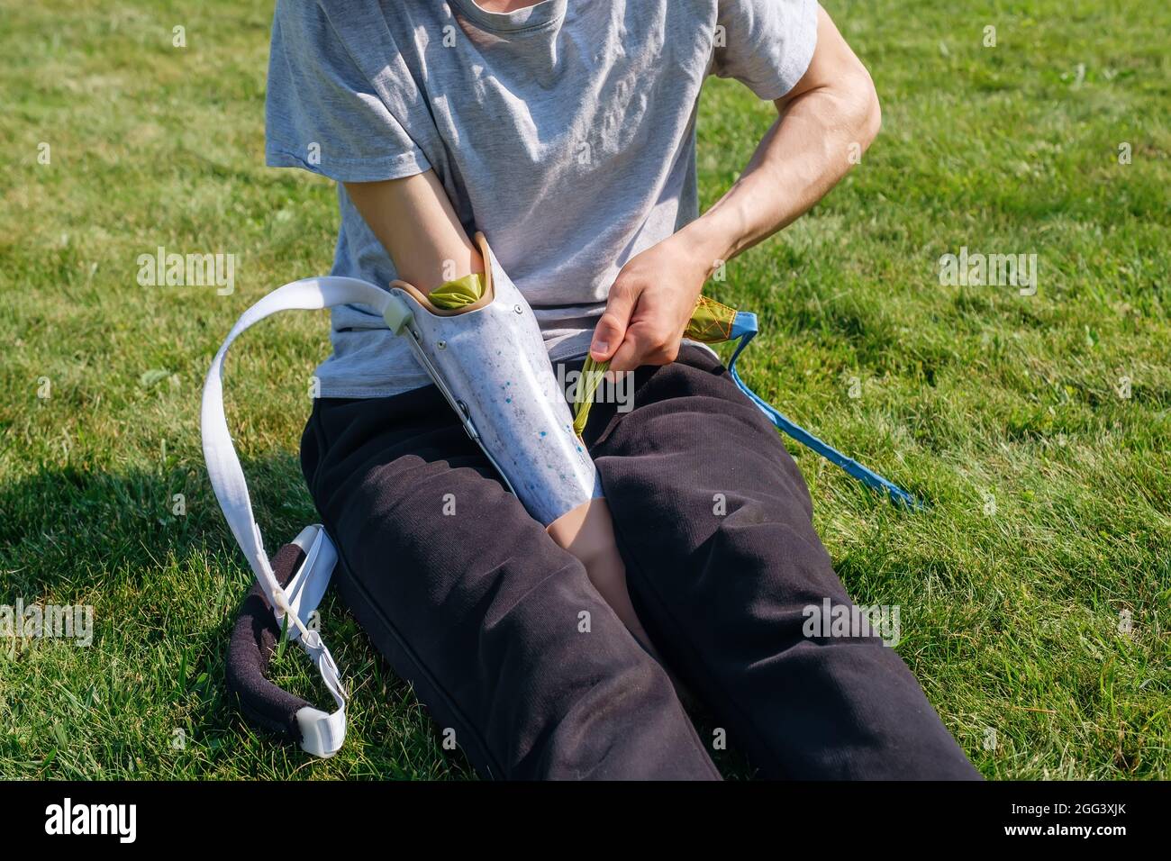 Young man with disability puts on prosthesis in yard Stock Photo