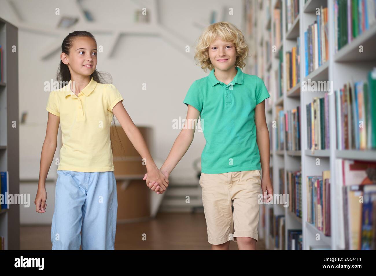 Two friends passing by bookshelves at a public library Stock Photo