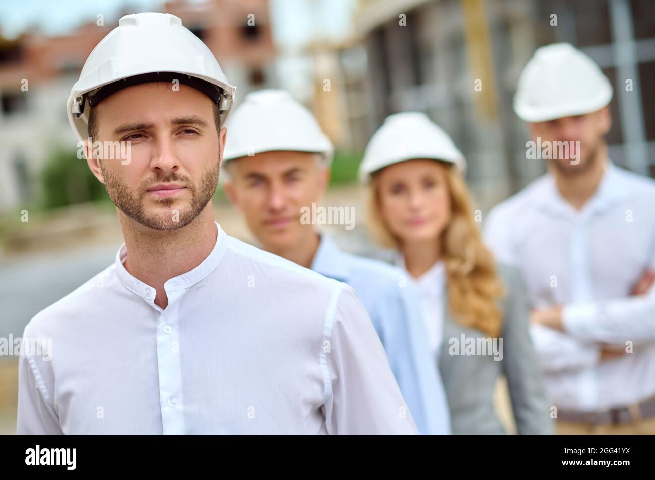 Serene construction worker and his three coworkers wearing protective helmets Stock Photo