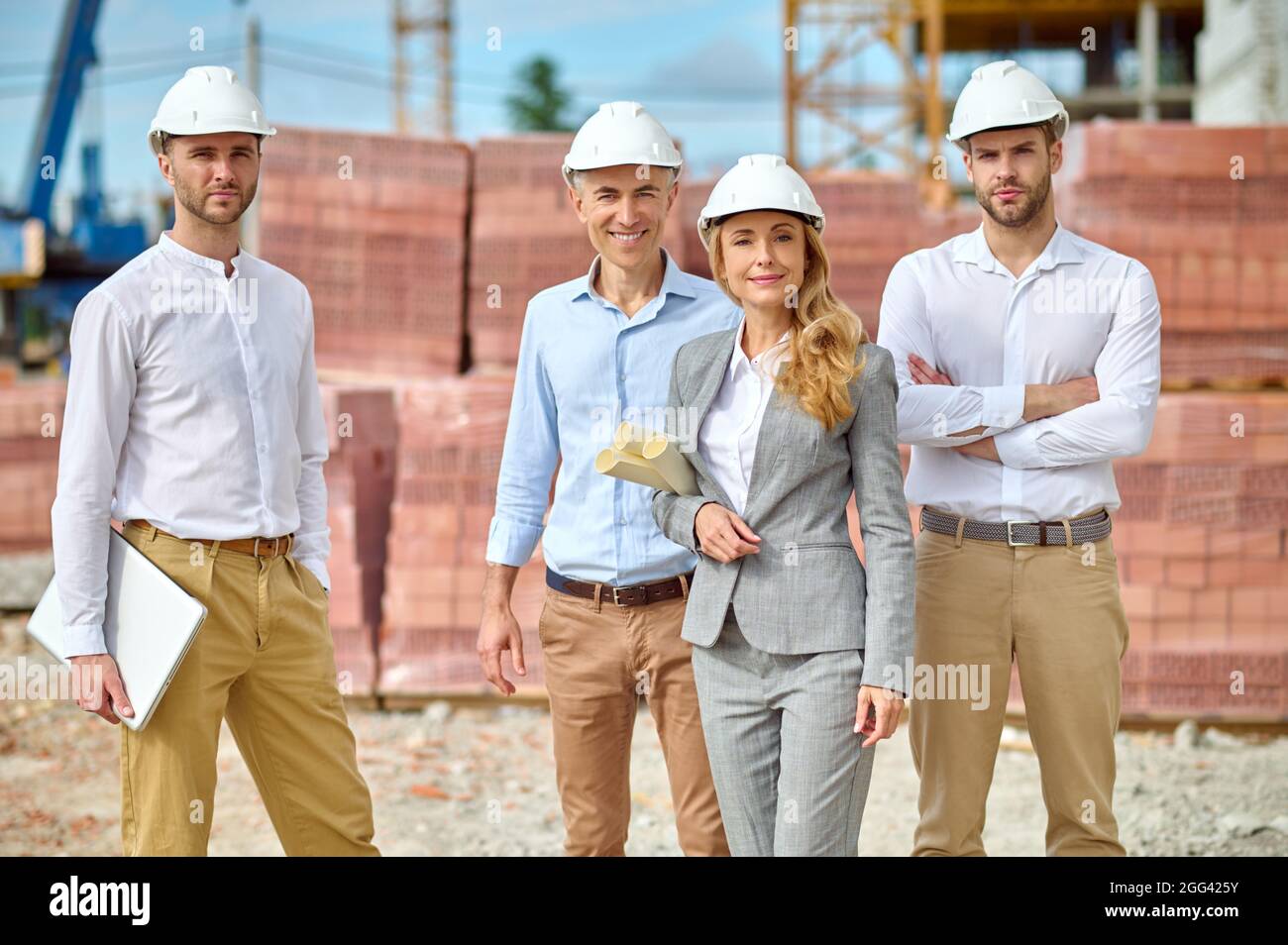 Confident lady supervisor and workers in hardhats standing outside Stock Photo