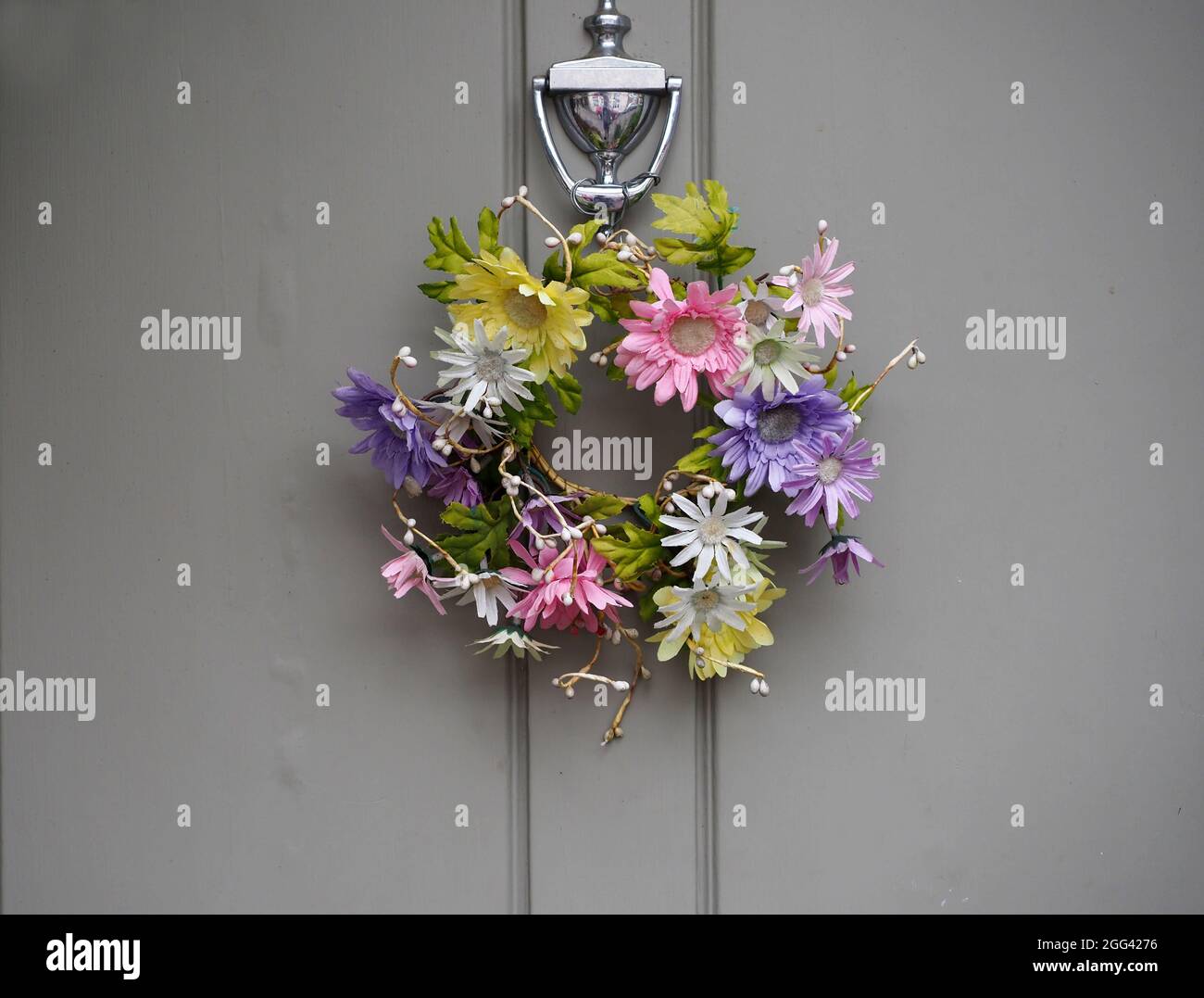 A galand of colourful flowers hanging from a grey door Stock Photo