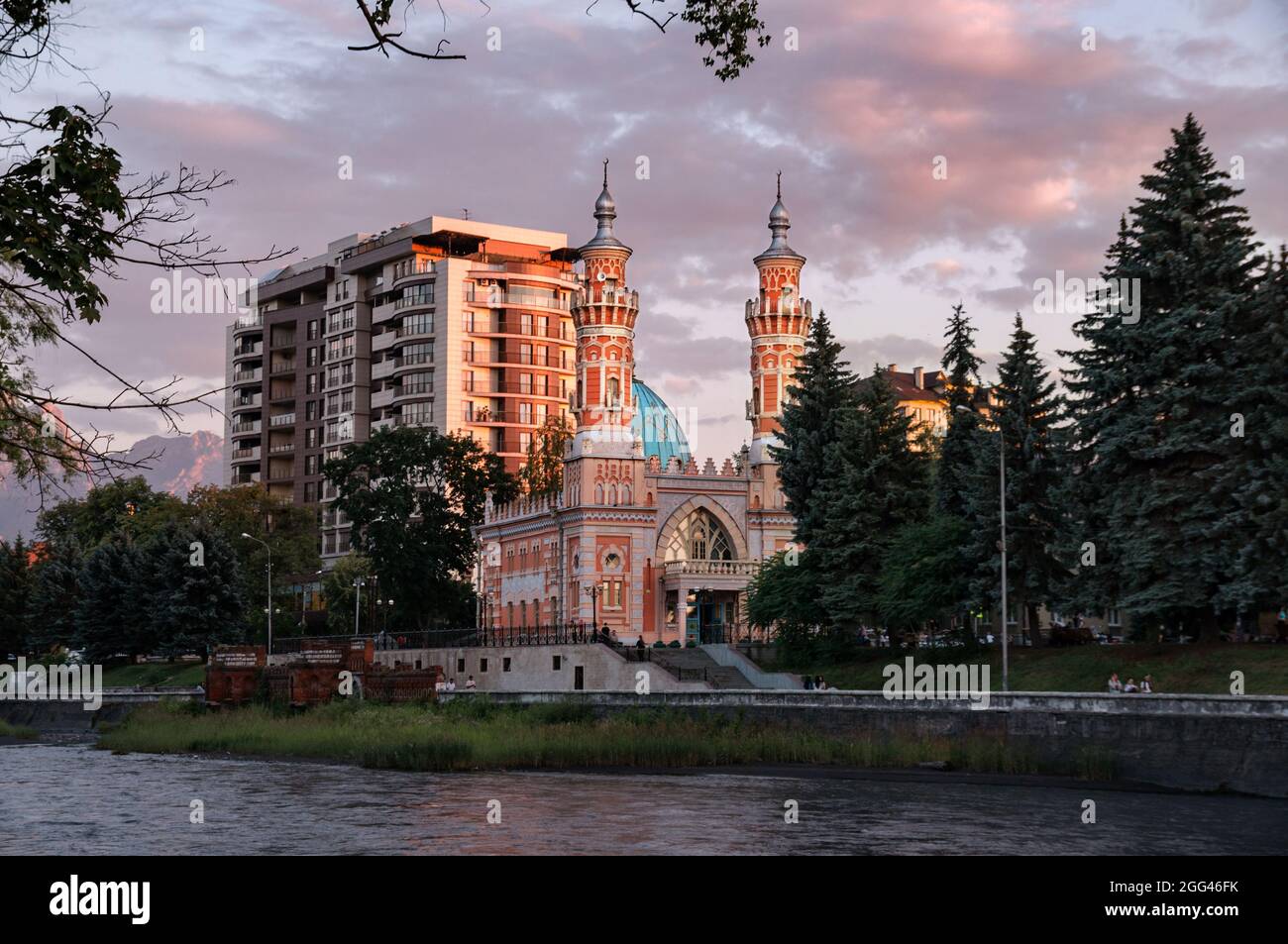 View on Minarets of Sunni Mukhtarov Mosque lit with warm sunset rays in front of pink gray clouds of summer evening sky on the bank of Terek river in Stock Photo