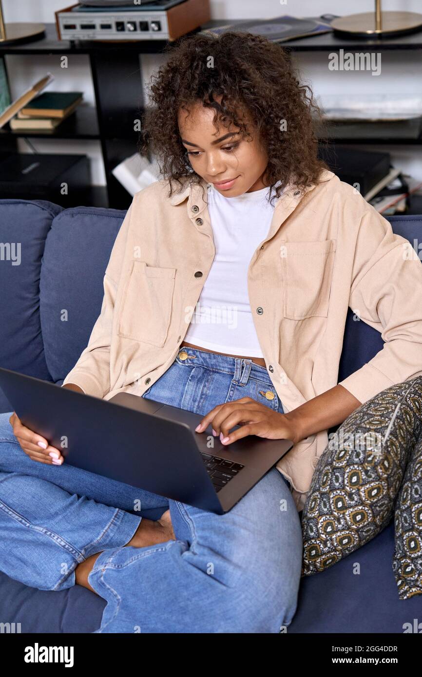 African American female student sitting on soft sofa at home using pc ...