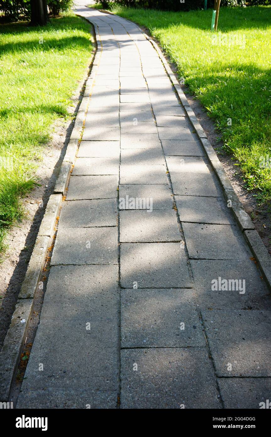 Vertical shot of a tiles footpath surrounded by freshly mowed green ...