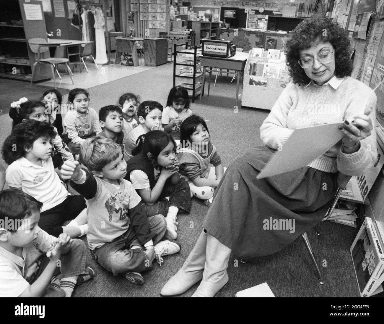 Austin Texas USA, circa 1991: Hispanic kindergarten teacher reads to Hispanic students sitting on floor in front of her in bilingual classroom at Sanchez Elementary School. ©Bob Daemmrich Stock Photo