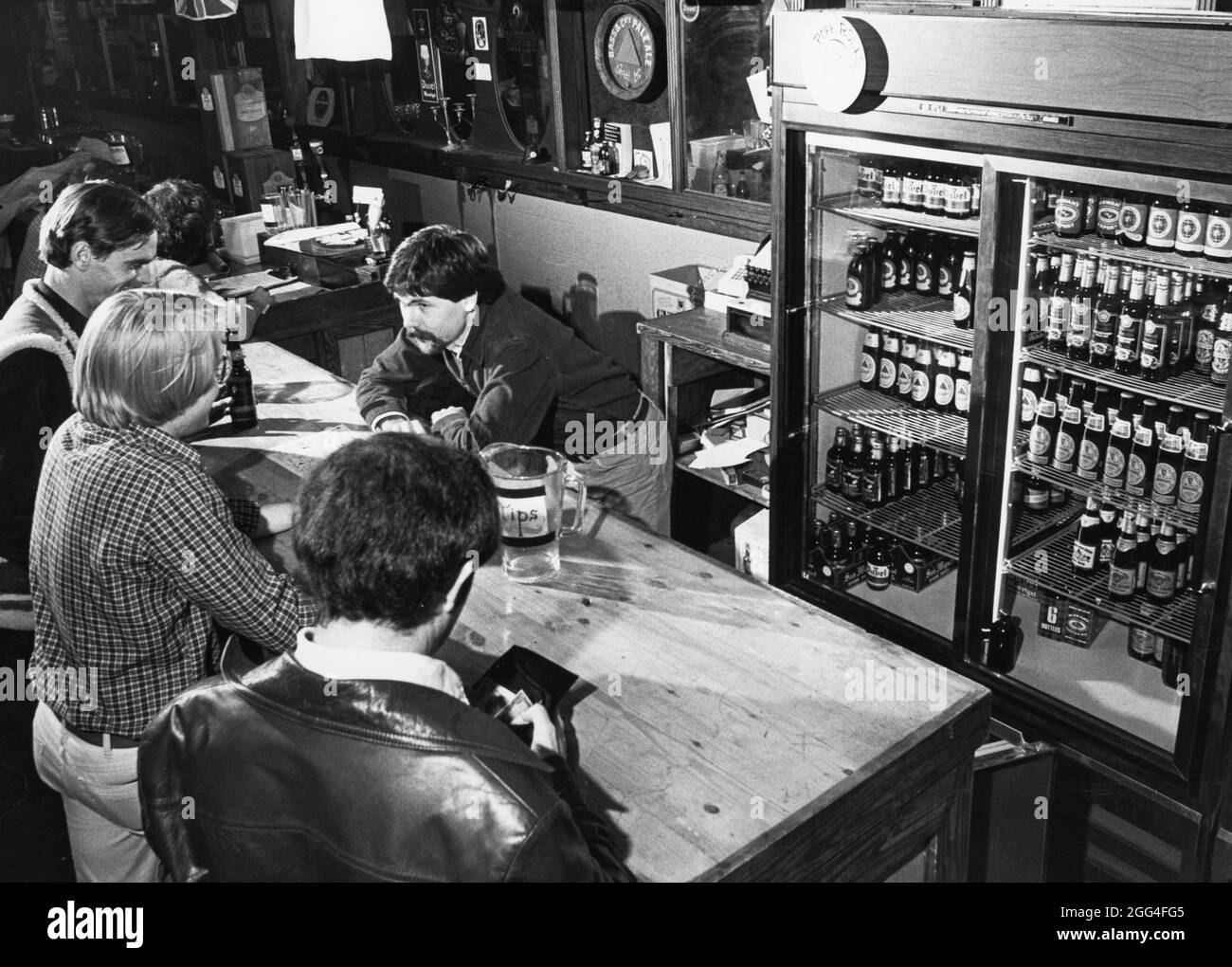 Austin Texas USA, circa 1984: Bartender and patrons at local bar on East Sixth Street, with many types of bottled beer available in cooler. ©Bob Daemmrich Stock Photo