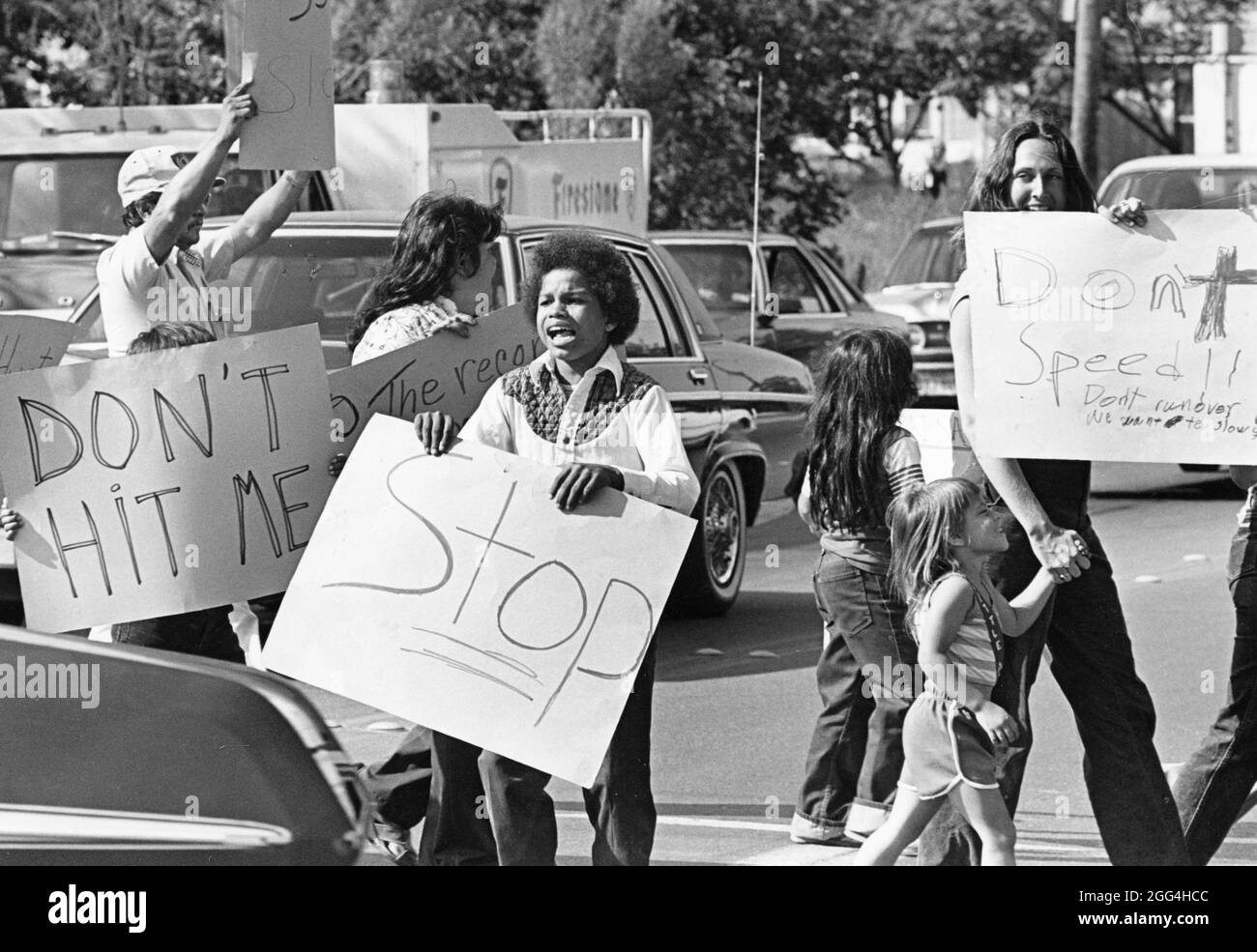 © 1990: Residents walk through traffic with hand-made signs protesting lack of traffic signals in their neighborhood that lead to cars driving too fast. Stock Photo