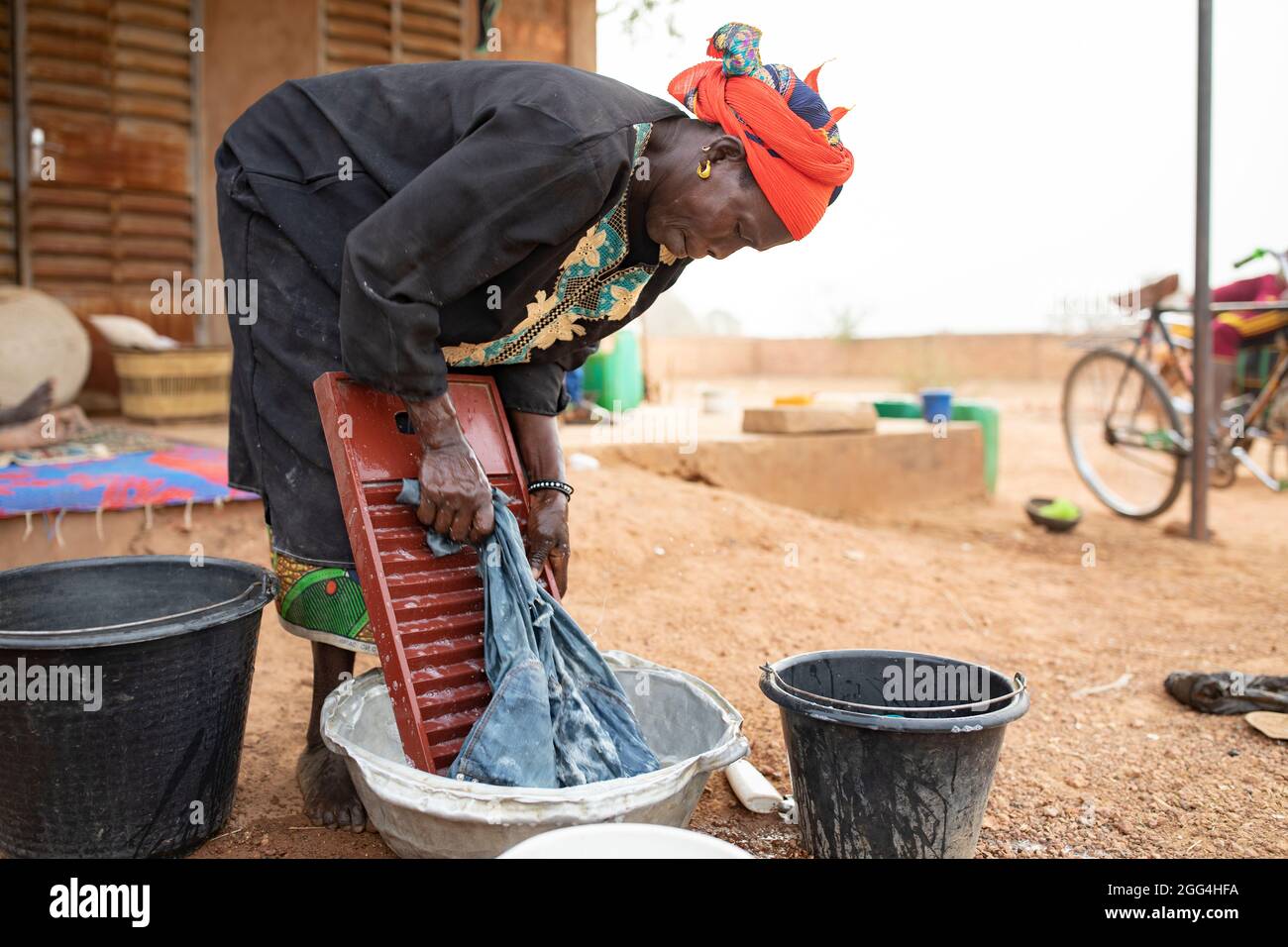 A woman washes clothes using a washboard and basin outside her home in ...