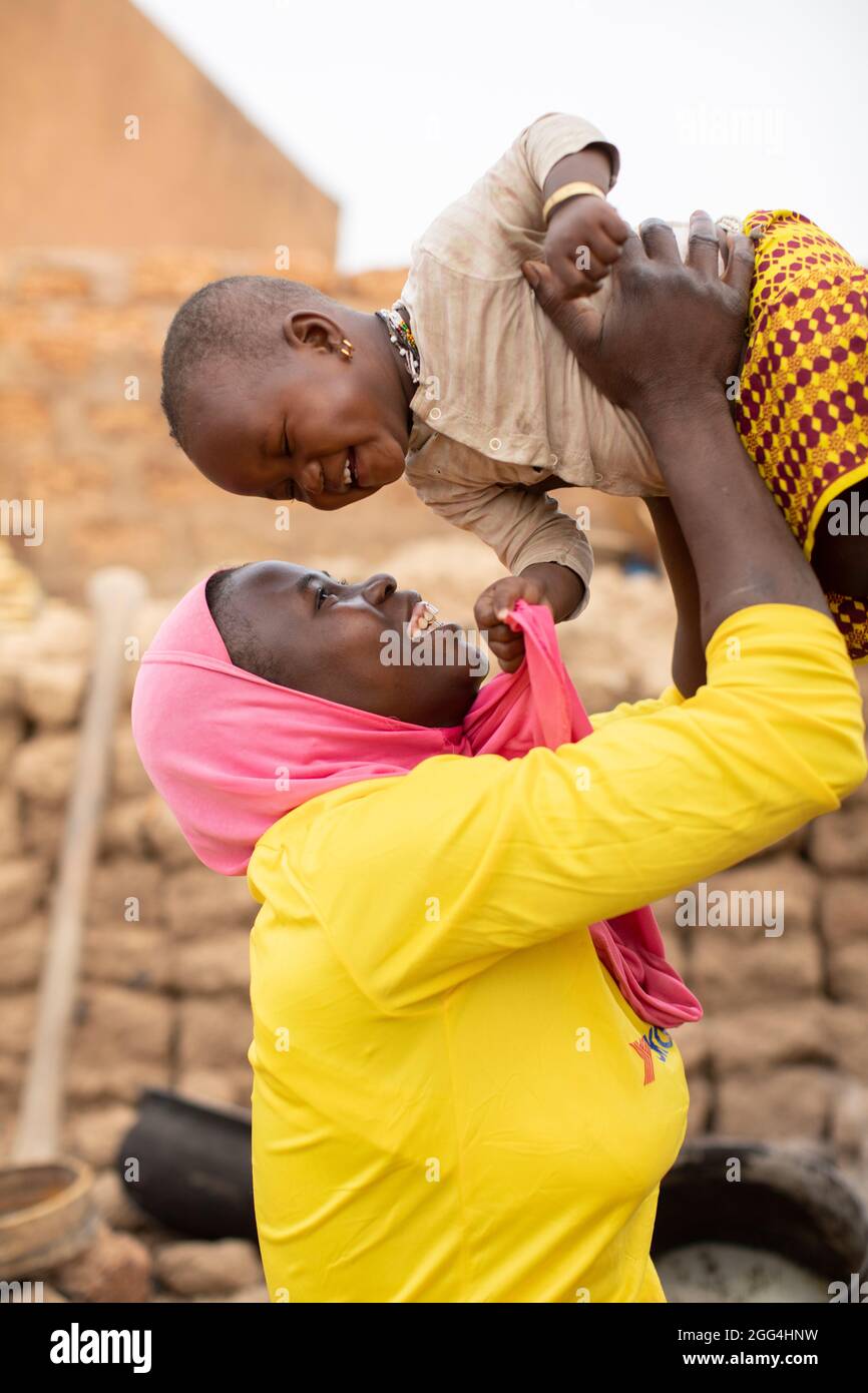 A young mother wearing an Islamic hijab lifts up her daughter and