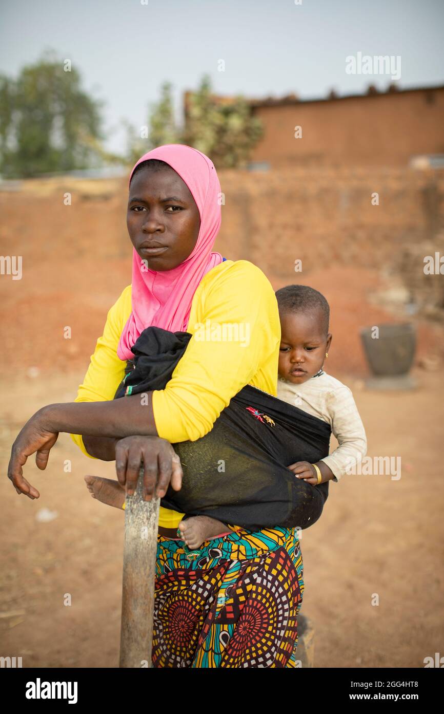 A young mother carries her baby daughter on her back in Kossi Province