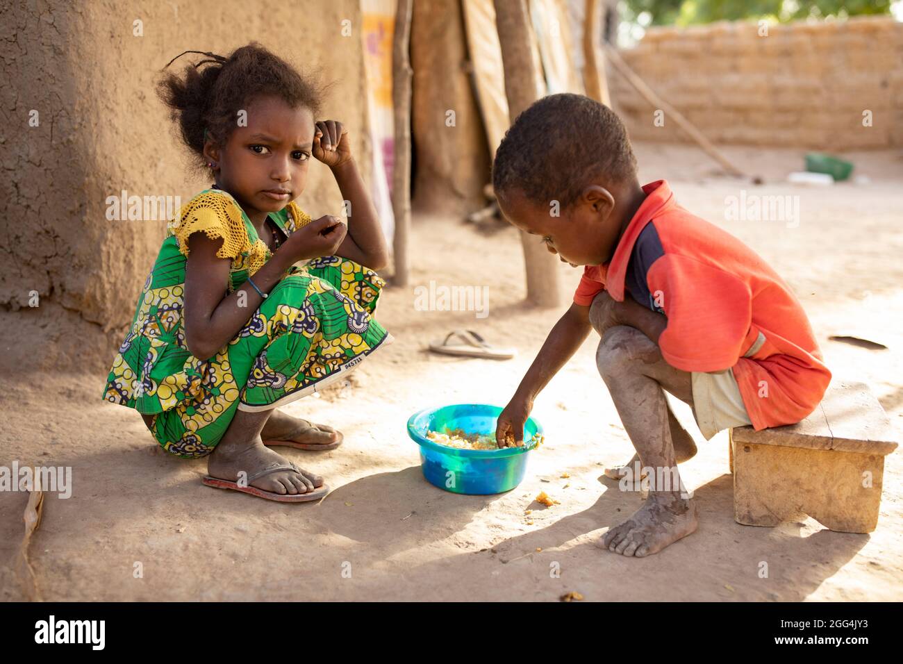Children eat out of a communal bowl with their hands outside their home ...