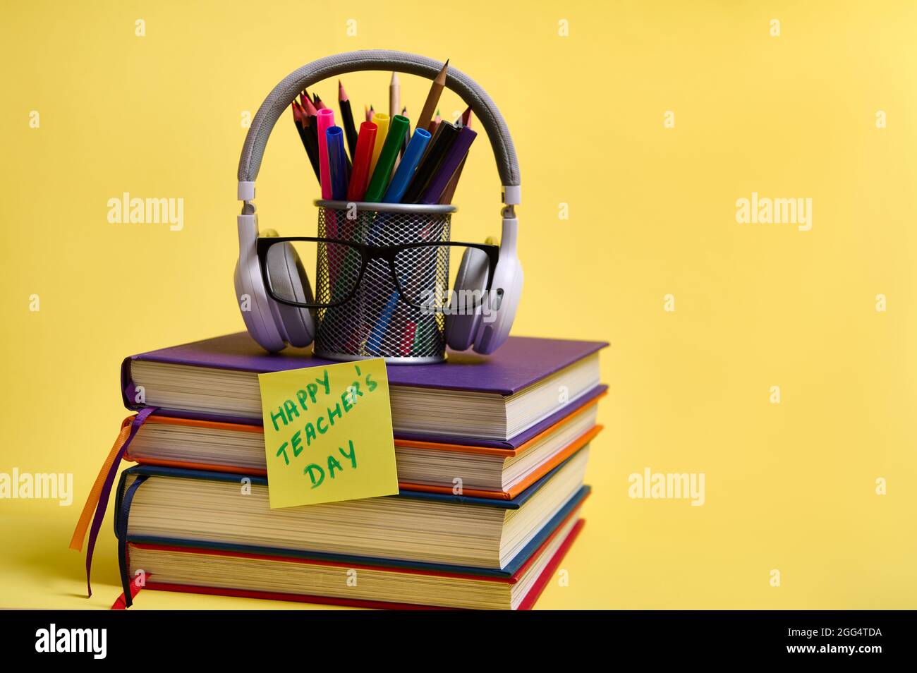 Composition from a stack of colorful books pencils glasses wireless headphones on a yellow background with copy space. Back to school concepts. Teache Stock Photo