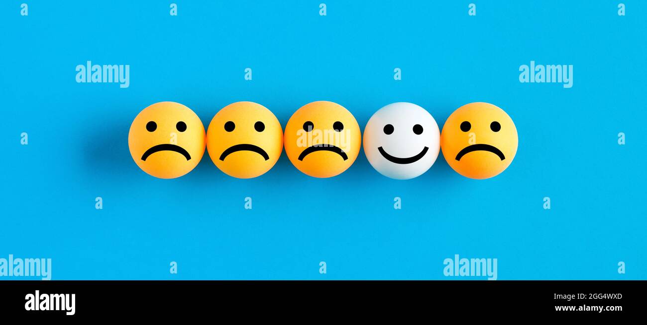One happy face emoticon among unhappy or sad face emojis in a row. Customer satisfaction or one happy client concept. Stock Photo