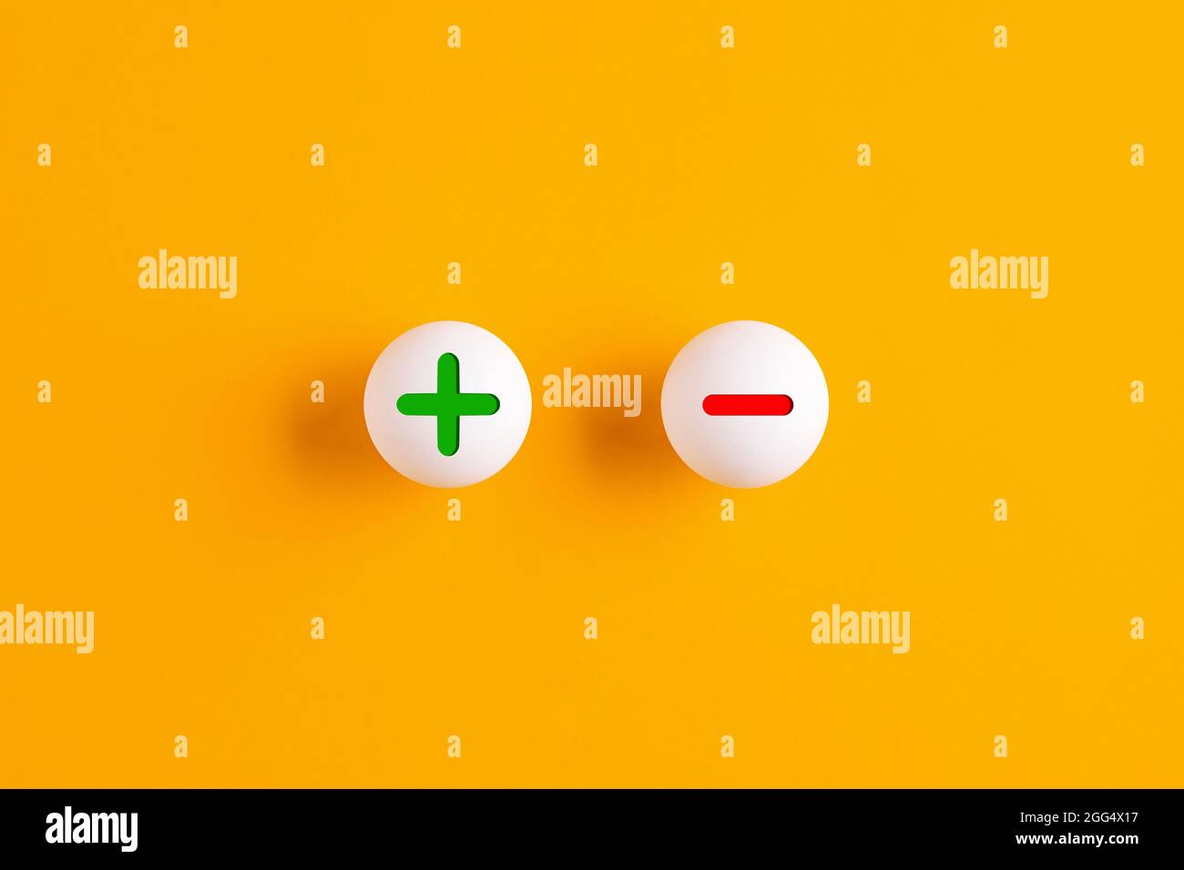 Plus and minus signs on table tennis balls on yellow background. Stock Photo