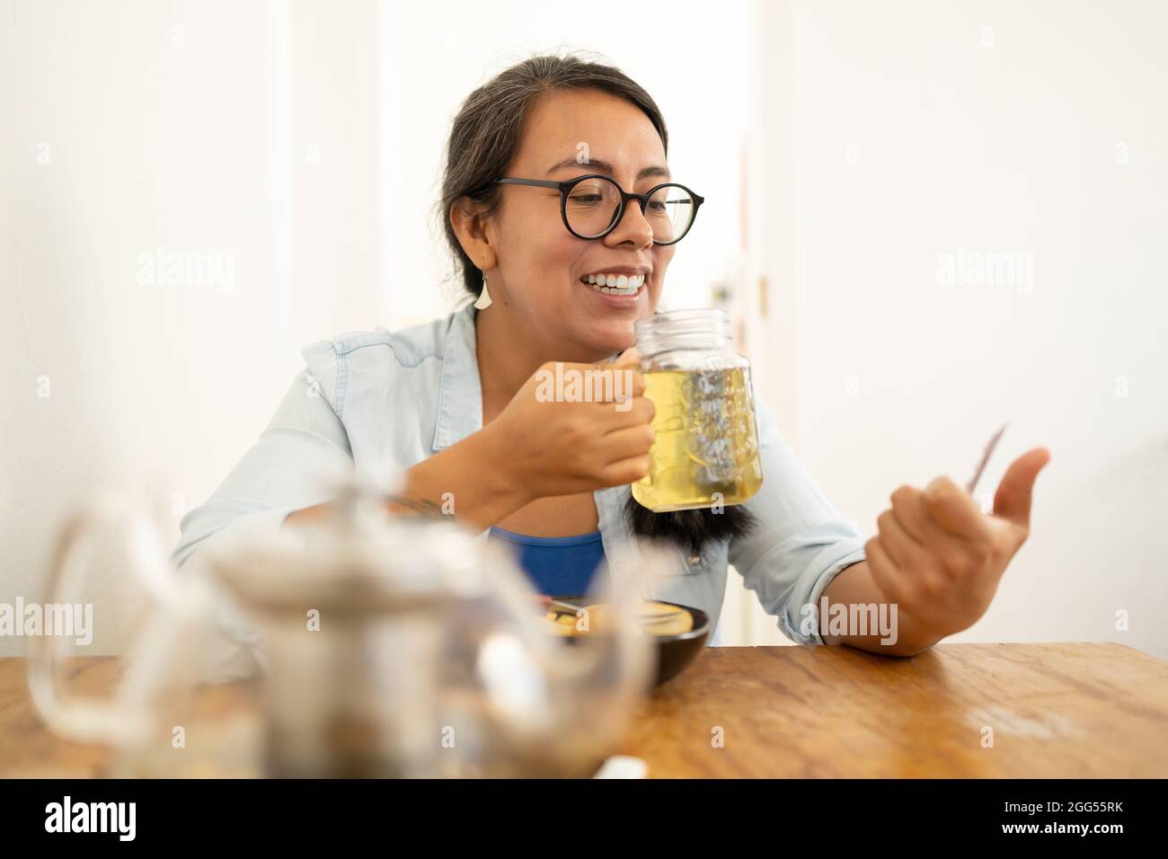 Beautiful Mexican female sitting in the kitchen texting and drinking tea Stock Photo