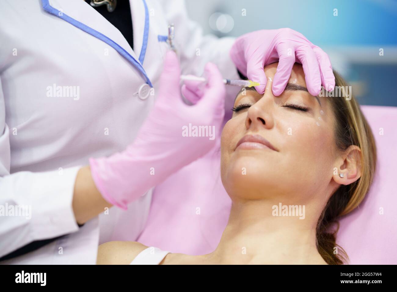 Aesthetic doctor injecting botulinum toxin into the forehead of her middle-aged patient. Stock Photo