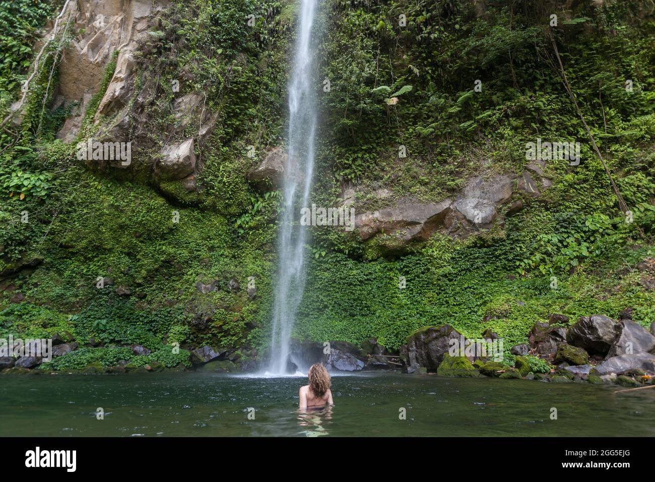 Girl in remote freshwater lagoon under waterfall Stock Photo