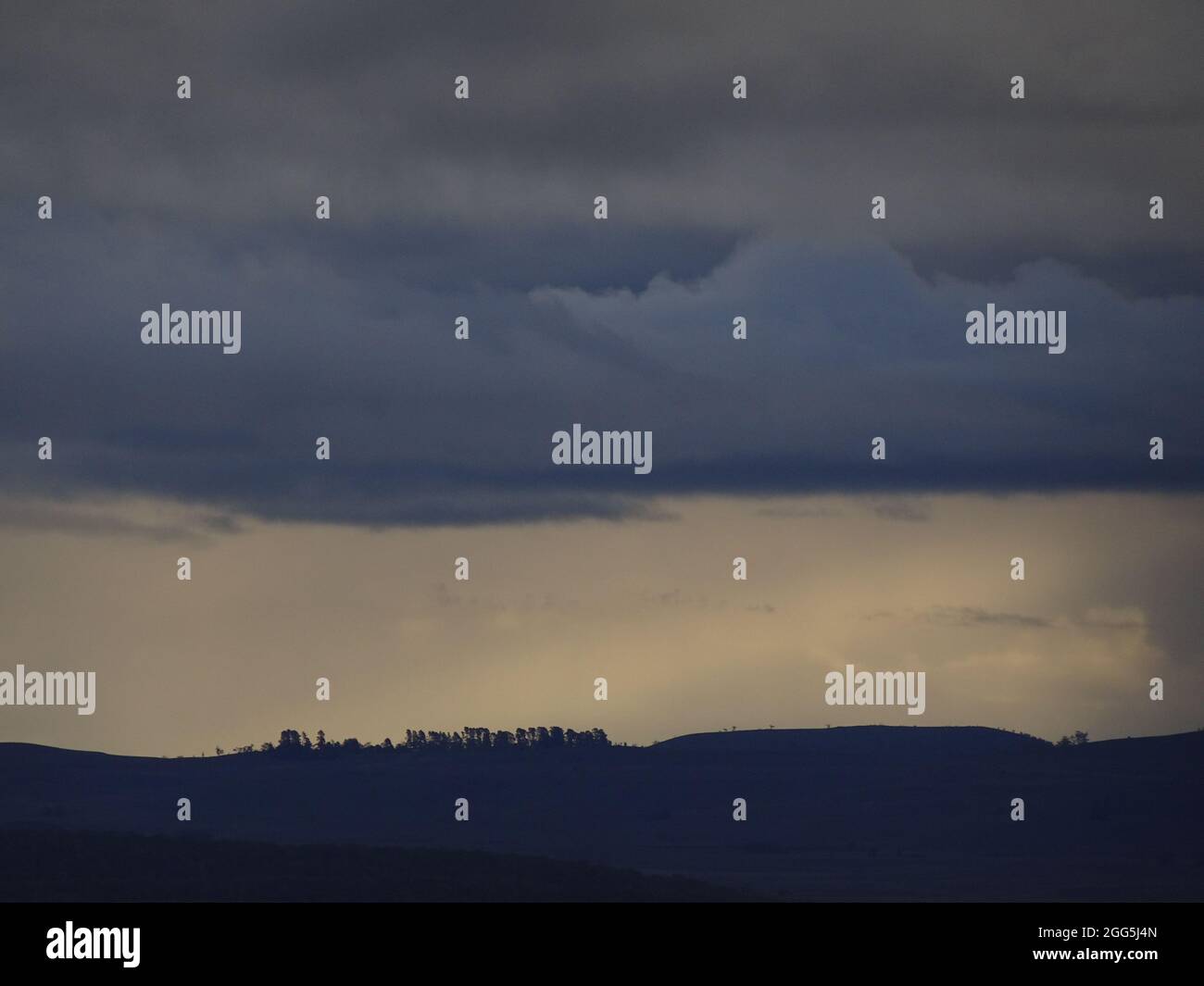 Silhouetted sky line of hills with trees against dark clouds Stock ...