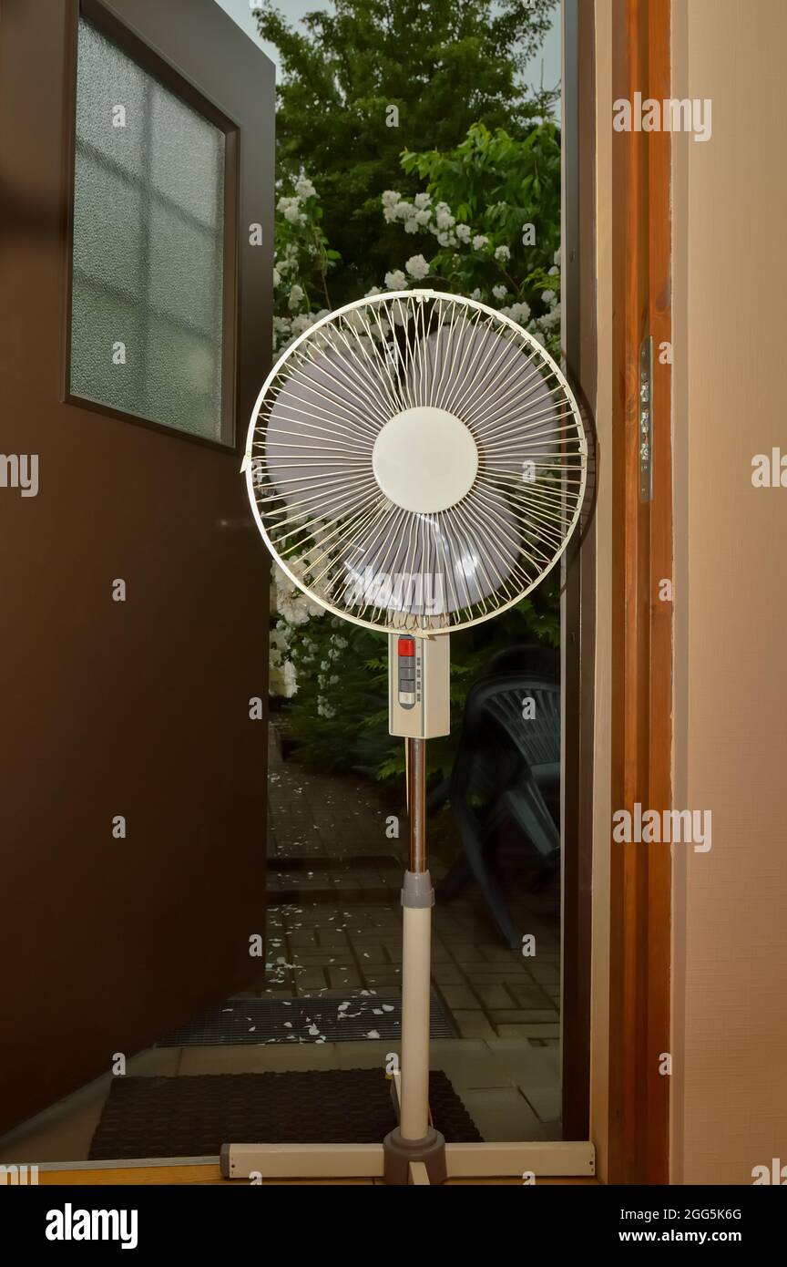 Electric floor fan stands at the door of the house for cooling in hot weather Stock Photo