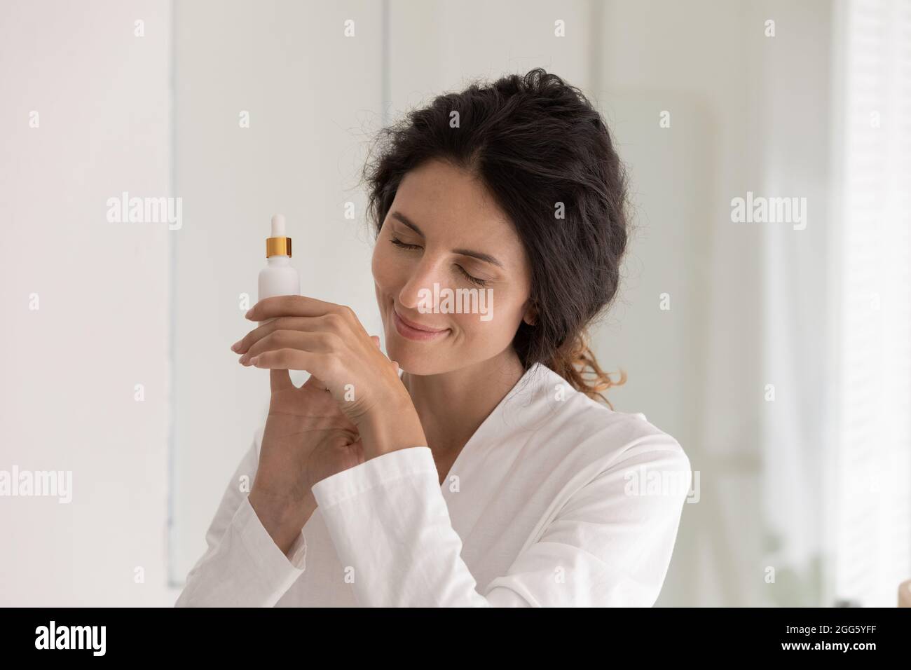 Peaceful happy young woman applying oil perfume on hands. Stock Photo