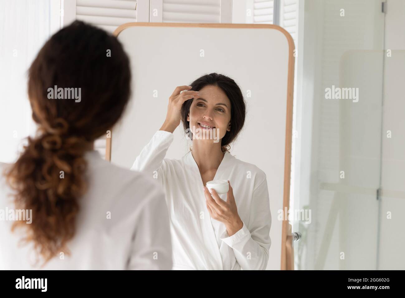 Happy young woman applying moisturizing cream on face. Stock Photo