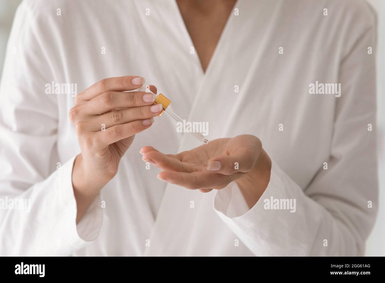 Close up young woman in bathrobe applying serum. Stock Photo