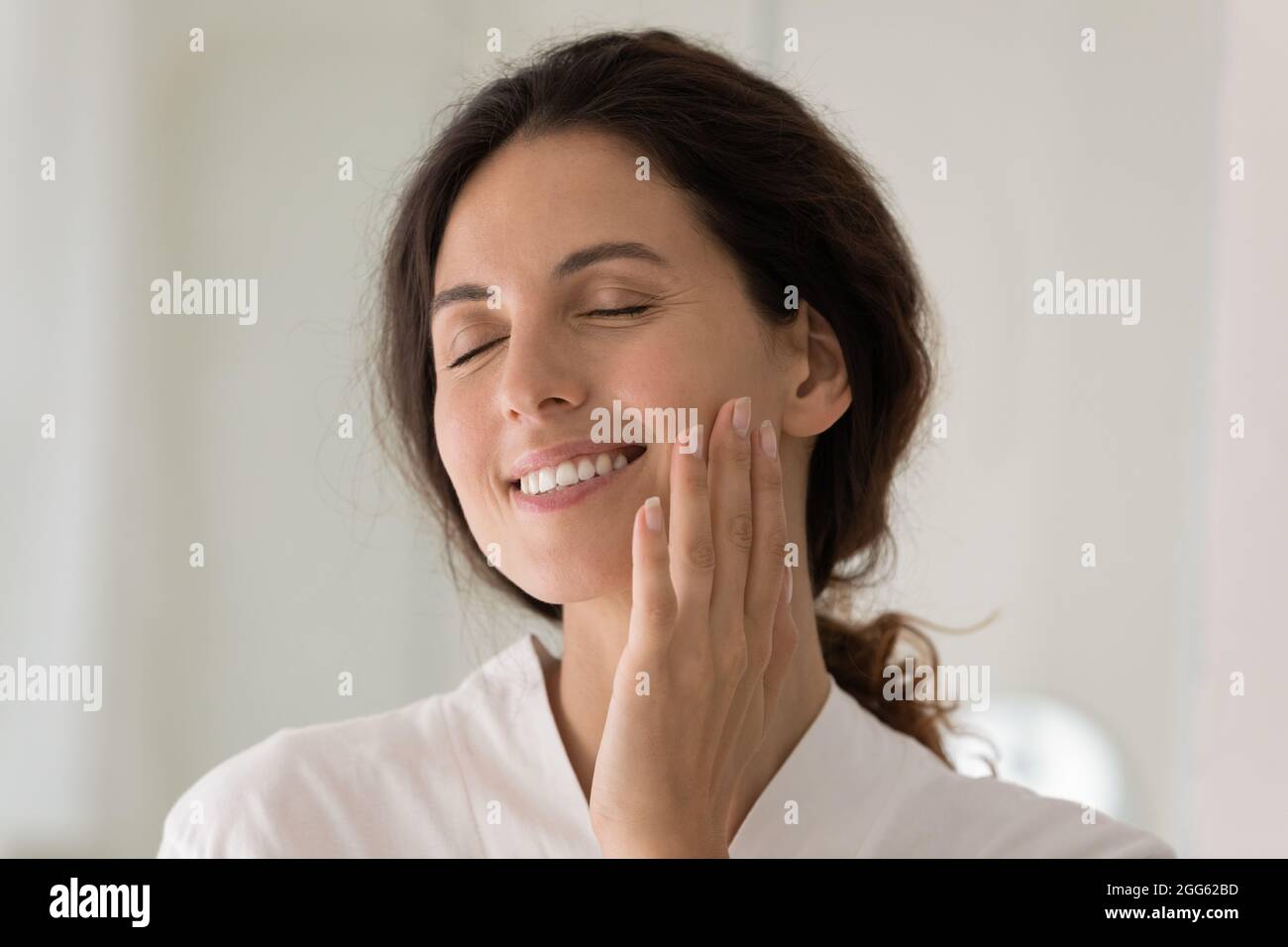 Smiling young woman touching soft facial skin. Stock Photo