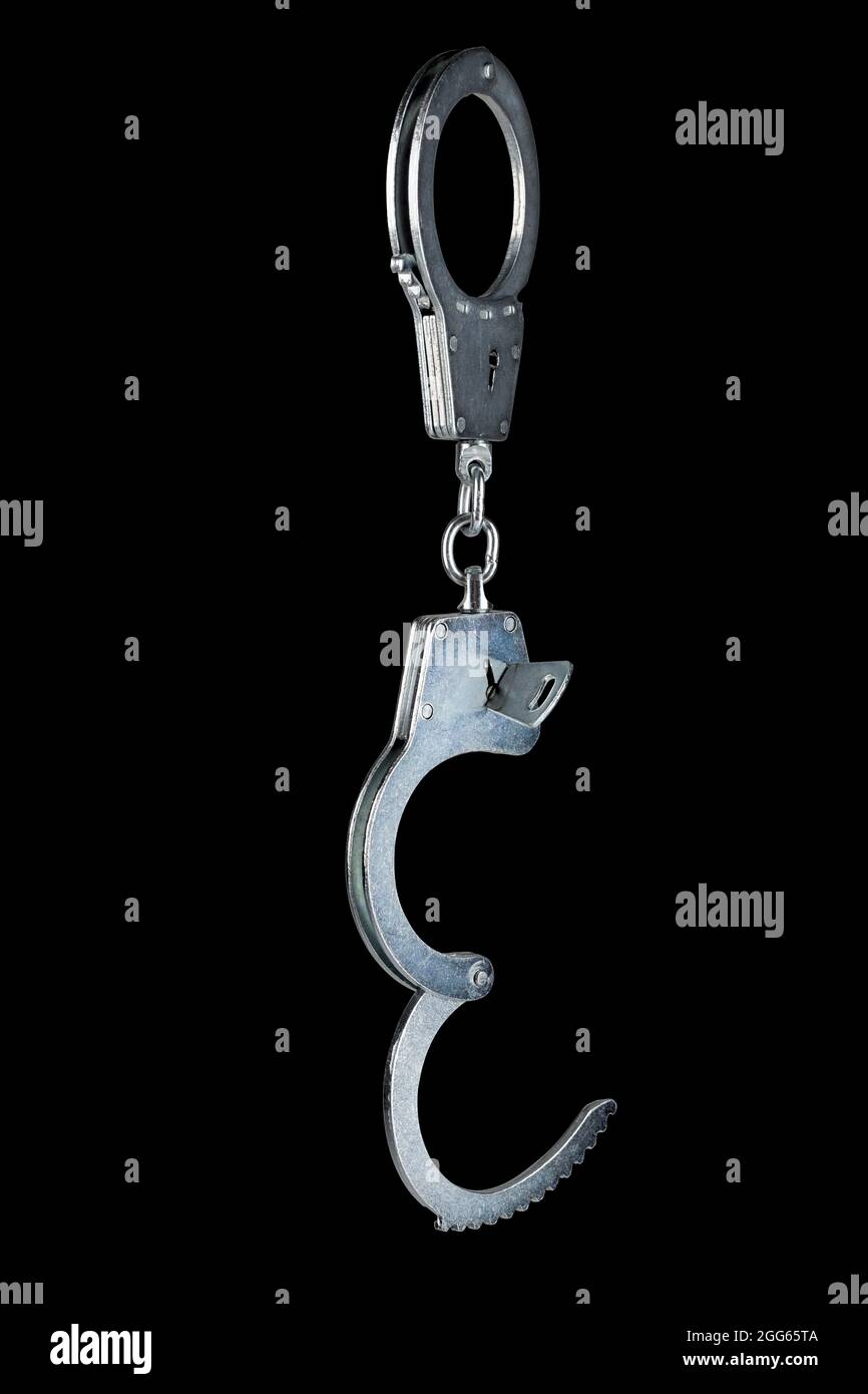 real zinc plated steel police handcuffs half-opened with key hanging vertically, isolated on black background Stock Photo