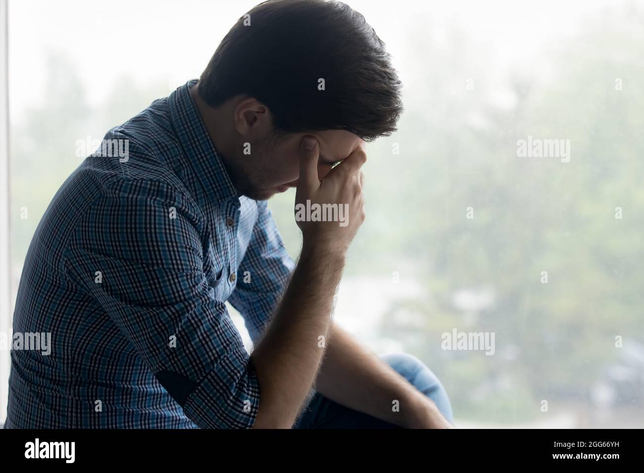 Depressed frustrated millennial man touching head, covering face Stock Photo