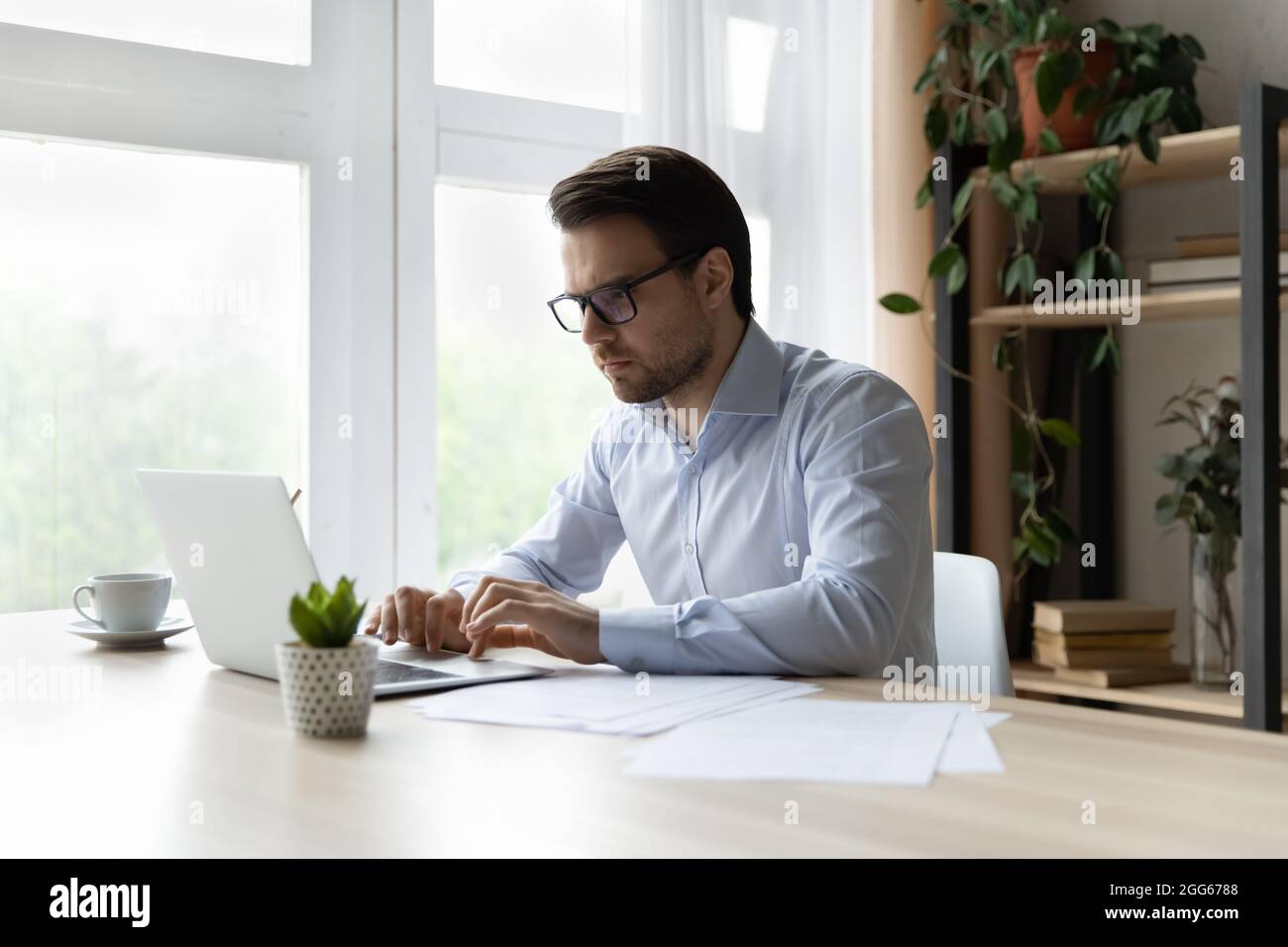 Serious millennial businessman working at laptop in office Stock Photo