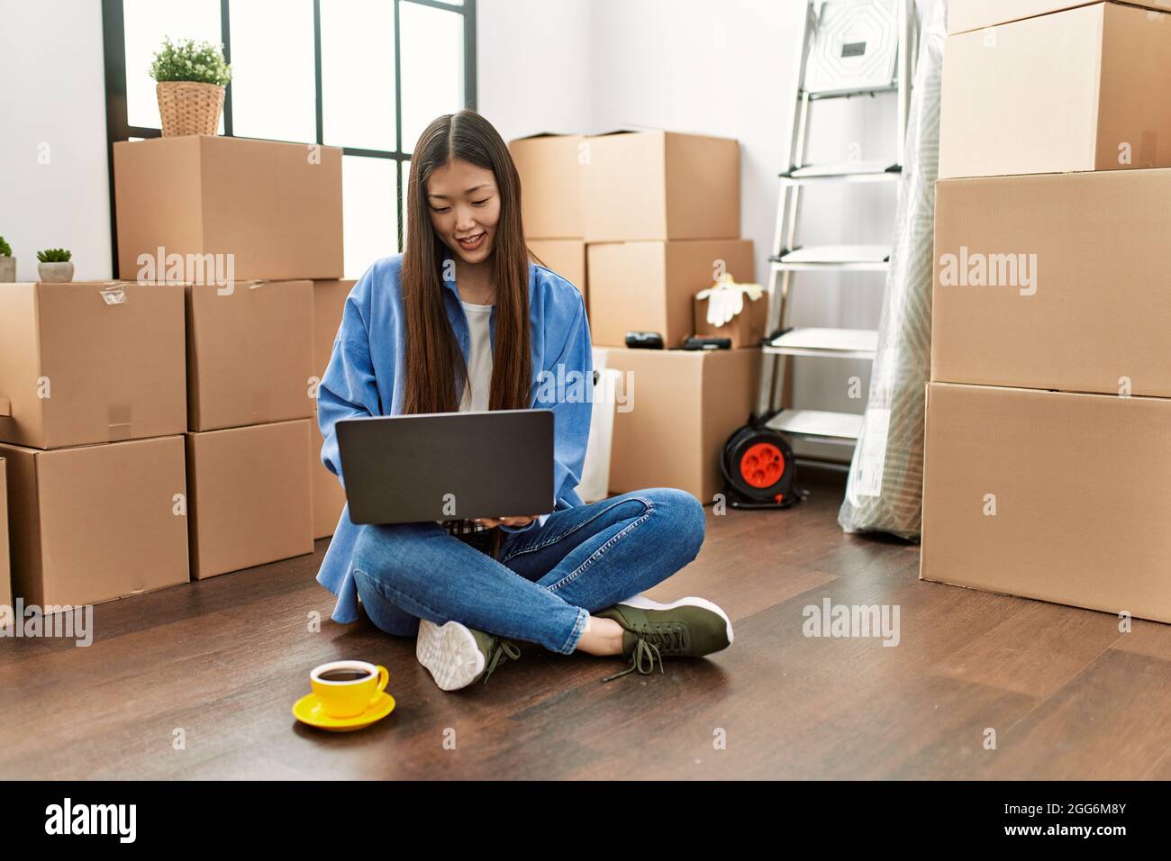 Young chinese girl smiling happy using laptop sitting on the floor at ...