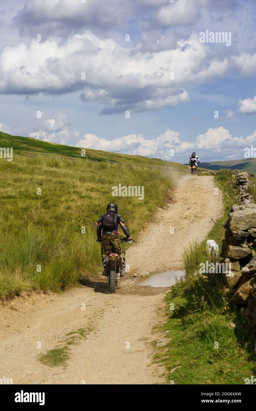 Two motorcyclists traveling off-road alongside a gravel track near Scar Reservoir, Upper Nidderdale, Lofthouse, North Yorkshire, England, United Kingdom. Stock Photo