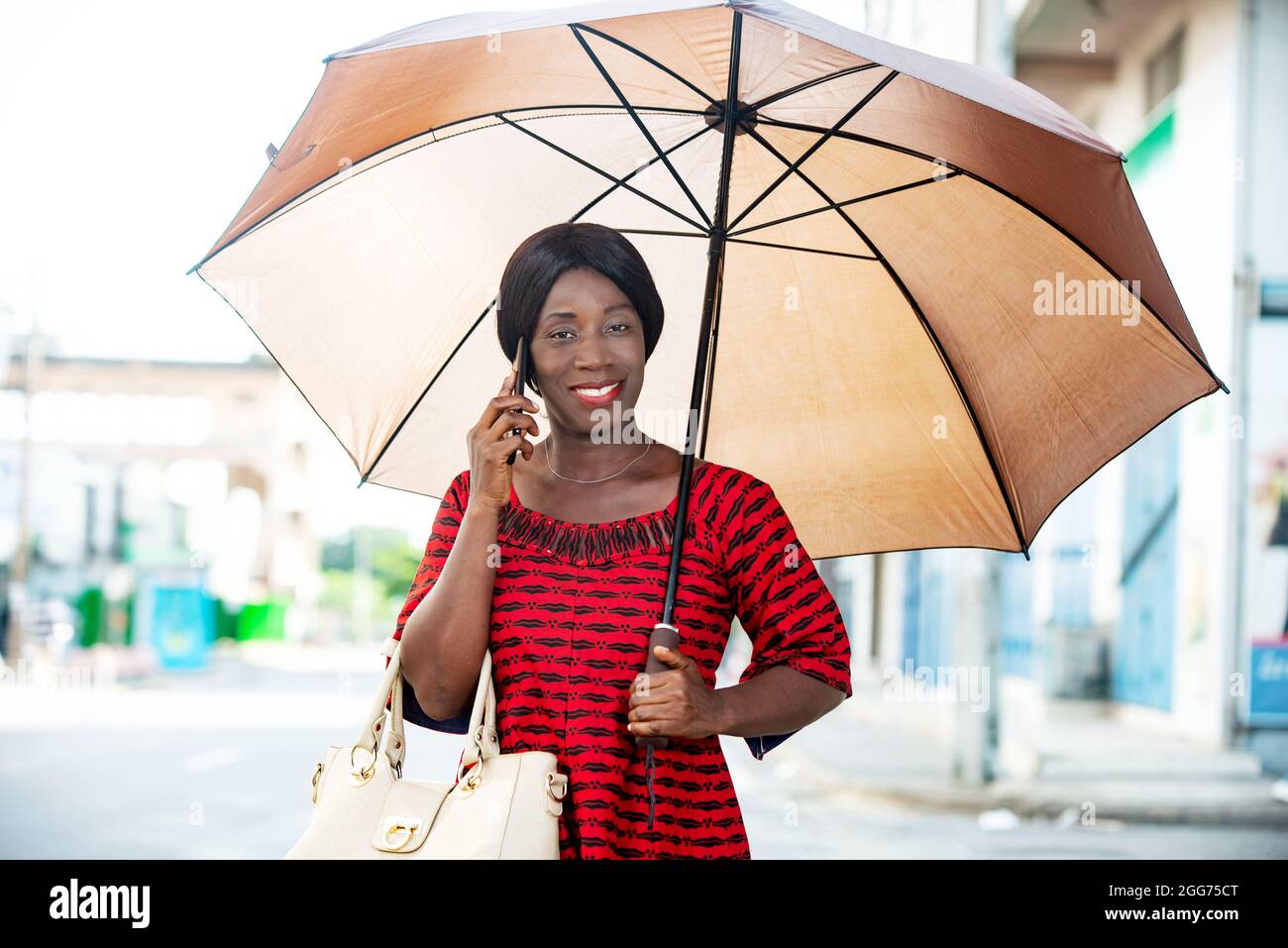 mature woman in traditional clothes standing talking on mobile phone smiling with umbrella over her head. Stock Photo