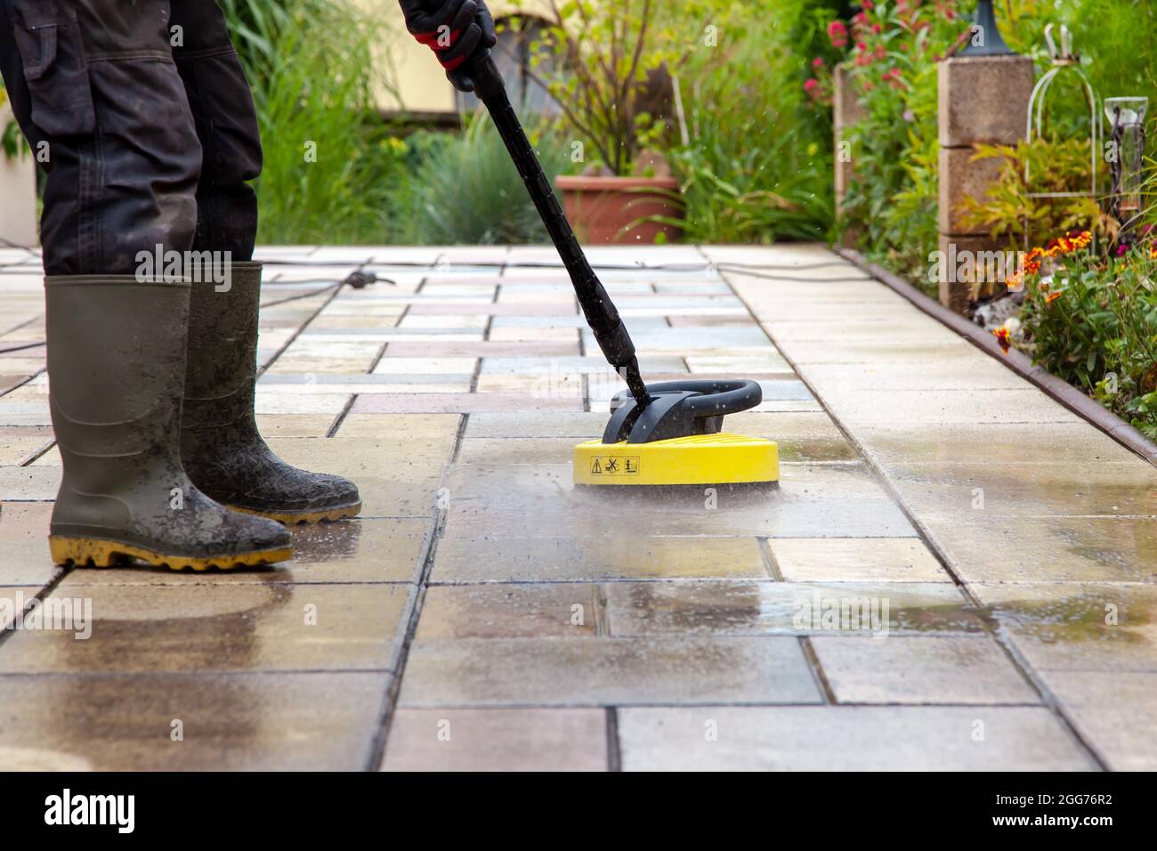 Cleaning stone slabs on patio with the highpressure cleaner. Person