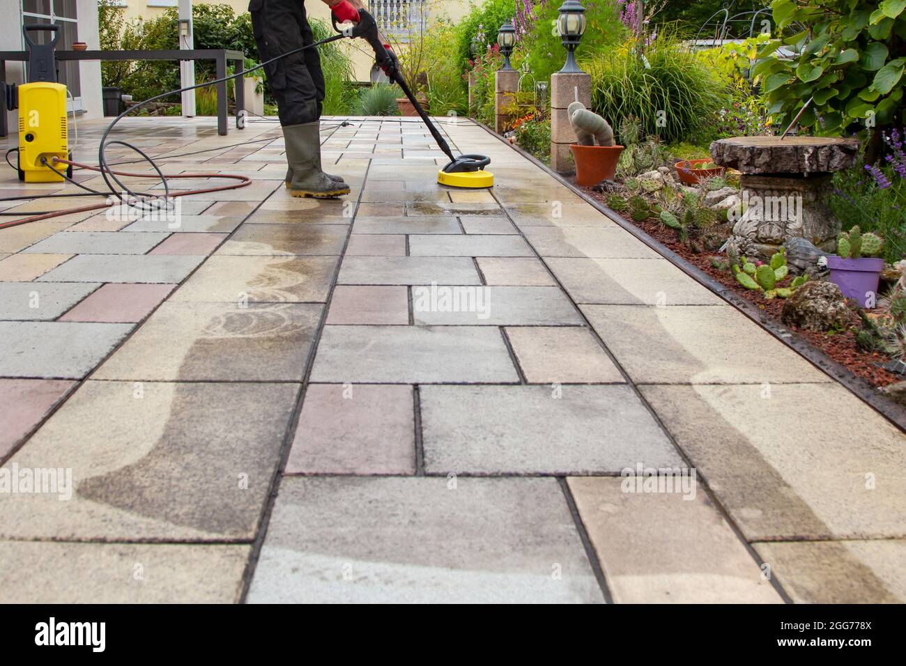 Cleaning stone slabs on patio with the highpressure cleaner. Person