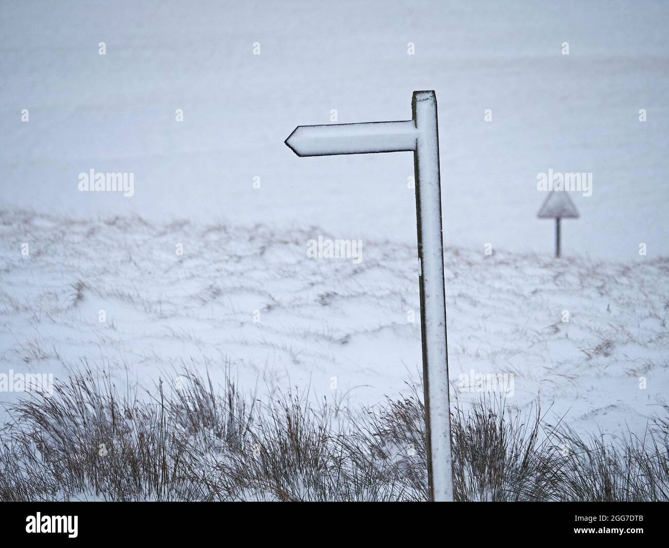 white out - finger post footpath sign & triangular road sign obliterated by snow on moorland in Winter storm Cumbria, England, UK Stock Photo