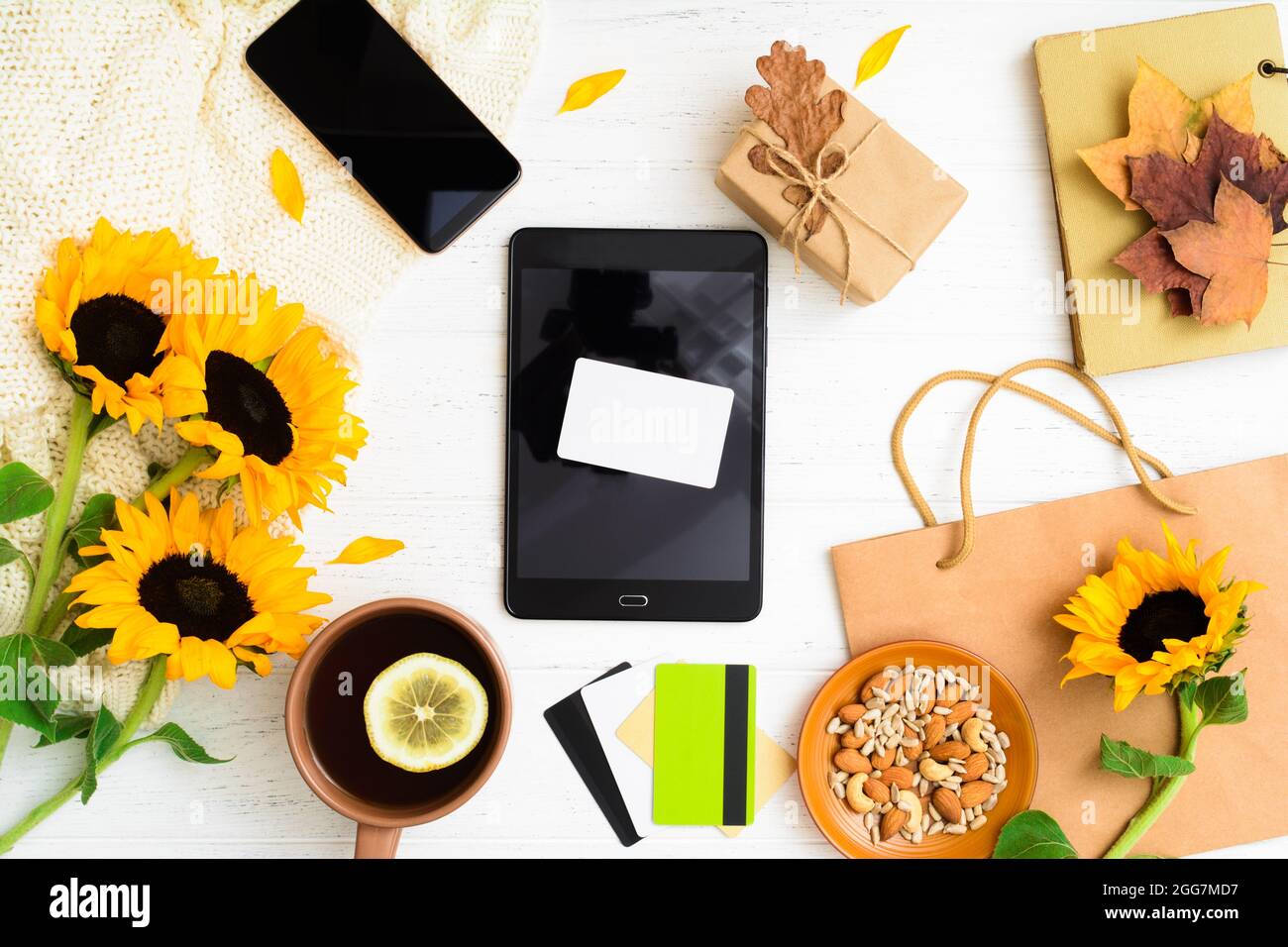 Empty bank card on tablet with gift, sunflowers, leaves, bag and tea with nuts Stock Photo