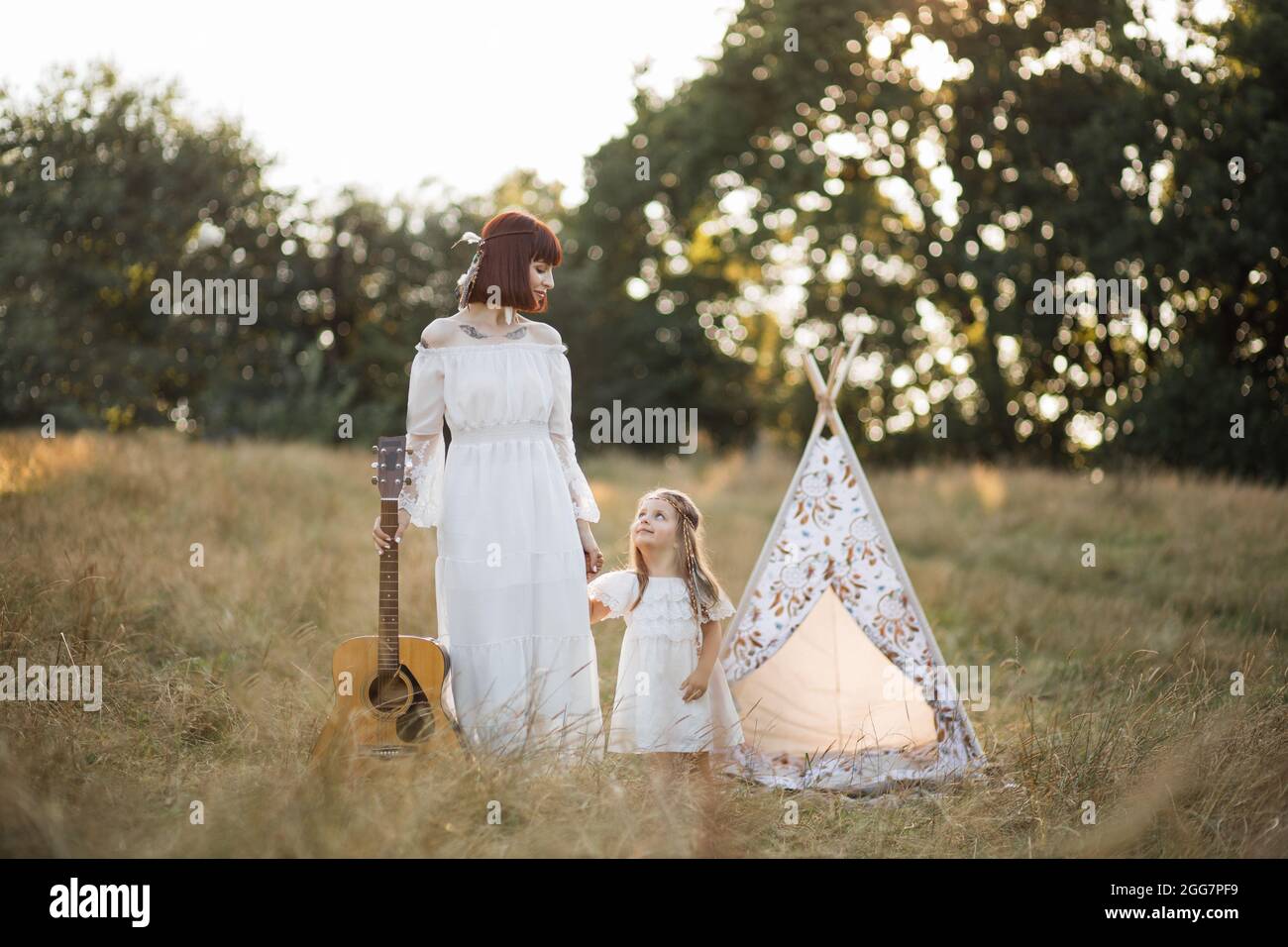Sunset atmosphere. Pretty stunning hippie boho family, mother and little  girl in white dresses and feathers