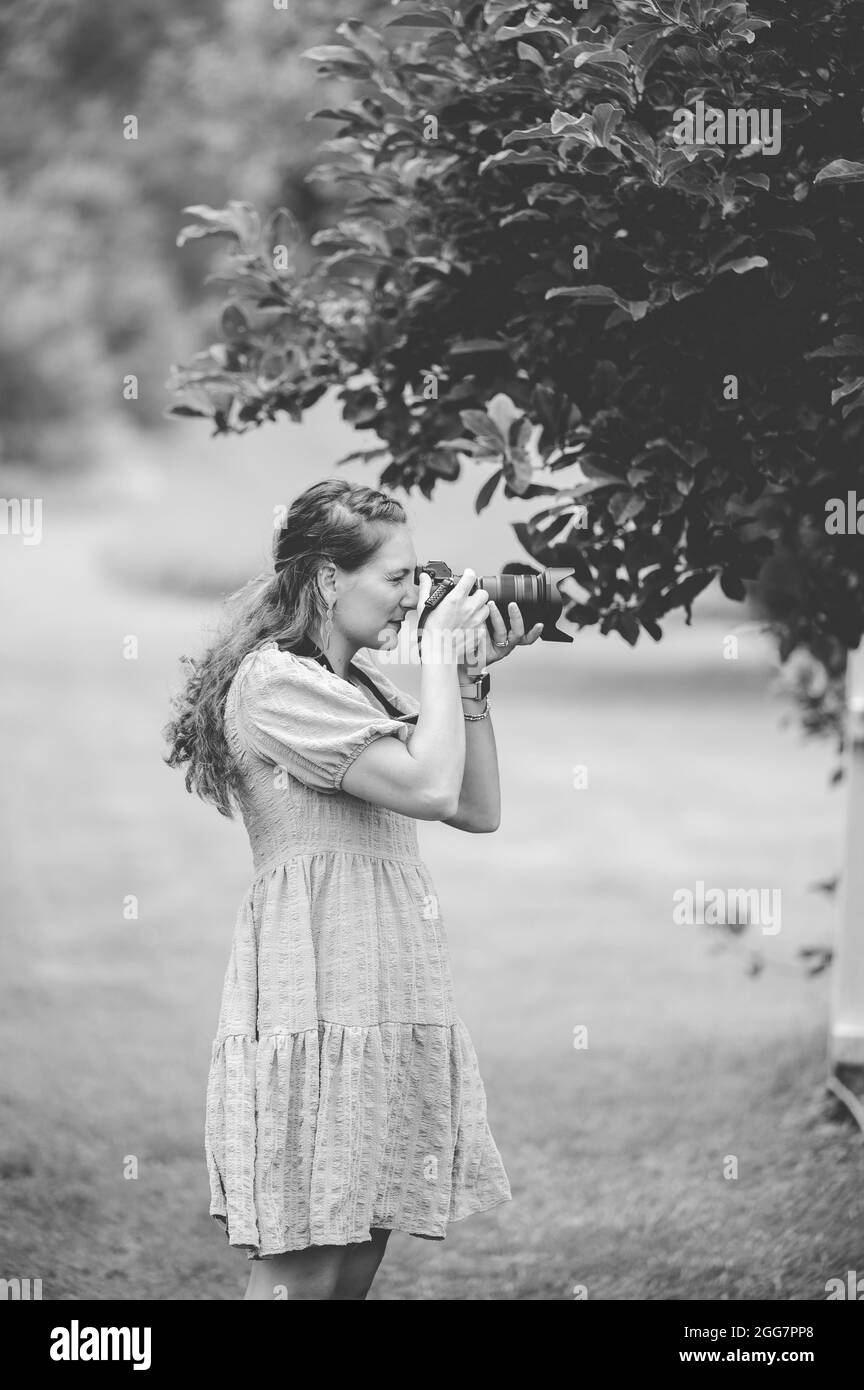 A grayscale shot of a female Caucasian photographer taking photos of nature at a park Stock Photo